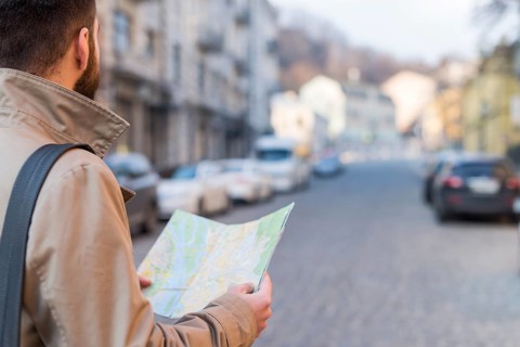 Male traveler holding map hand finding way city street