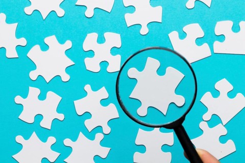 White jigsaw piece seen through magnifying glass blue white background
