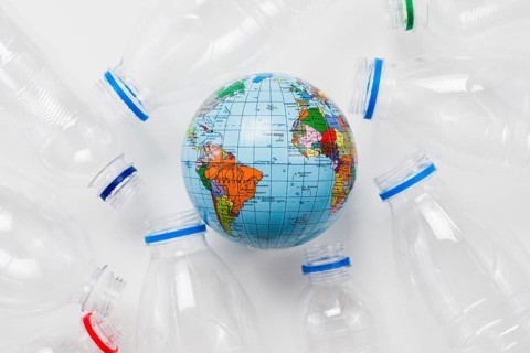 Earth globe surrounded plastic bottles grey table