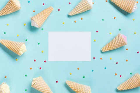 Overhead view waffle cones sprinkles surrounded near white blank paper blue backdrop