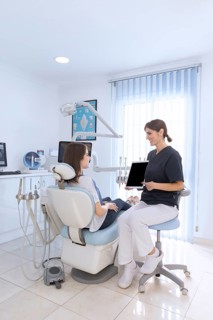 Female dentist pointing digital tablet screen patient sitting chair clinic
