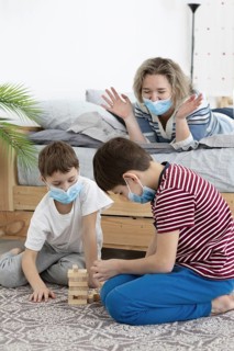 Children with medical masks playing jenga home with mother