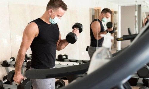 Man working out gym while wearing medical mask