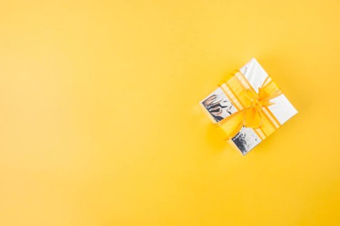 Silver gift box decorated with yellow ribbon yellow background
