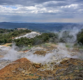 Steam rises above the colourful rubble deposits of the Biancane Geothermal Park and the town in the background