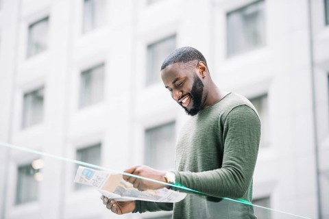 Smiling man reading newspaper near glass fence