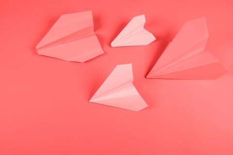 Coral pink paper airplane colored background