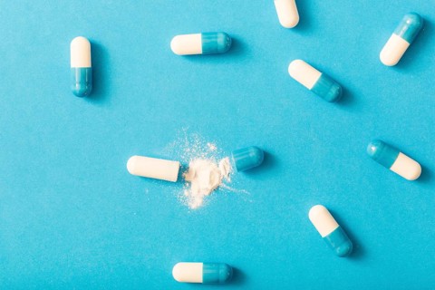 Split open capsule with white powder blue background