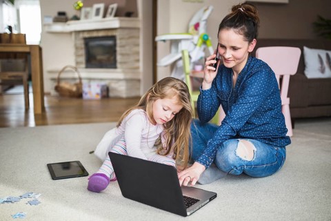 Woman sitting with her daughter talking cellphone while using laptop