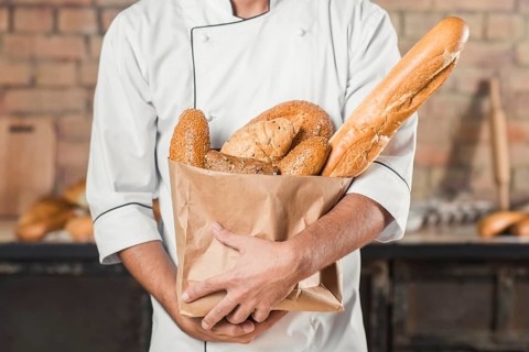 Mid section male baker holding different type breads paper bag