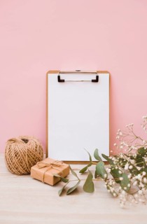 White paper clipboard with spool gift box baby s breath flowers wooden desk against pink background