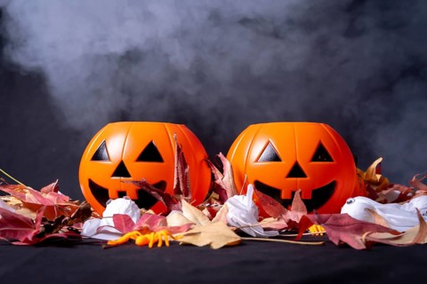 Detail of Halloween pumpkins over red autumn leaves and ghosts with smoke on a black background