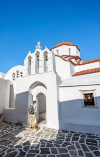 Young man with cat in front of archway with bells of Agios Antonios chapel and Greek Orthodox church Metamorfosi Sotiros