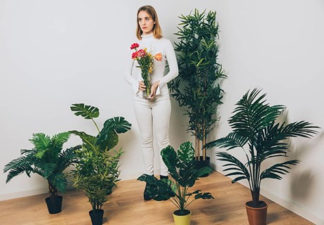 Thoughtful woman with flowers vase near green plant