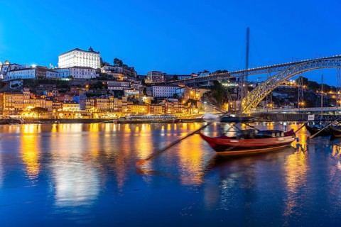 View over the traditional Rabelo boats on the Douro riverbank in Vila Nova de Gaia towards the old town of Porto and the Ponte Dom Luis I bridge at dusk