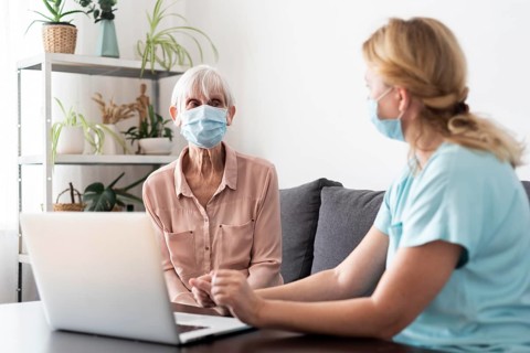 Female nurse older woman conversing laptop nursing home