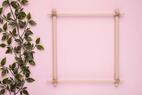 Wooden square frame with artificial green leaves pink backdrop