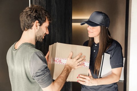 Young female courier delivering parcel man home