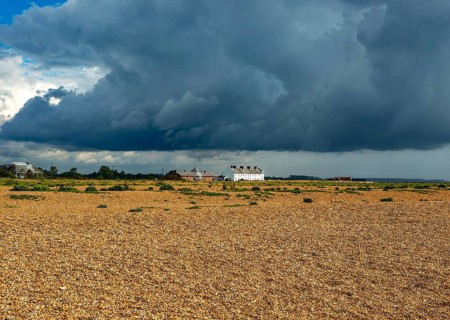 Dark rain clouds over houses and beach at Shingle Street
