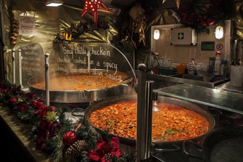 Large pans with simmering spicy chilli chicken for sale in stall during evening Christmas market in winter