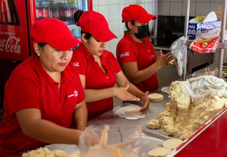 Woman rolling corn dough to make tortillas in gordita fast food cafe restaurant