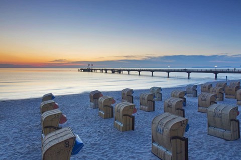 Roofed wicker beach chairs and wooden pier