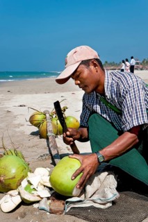 Burmese man opening coconuts on the beach