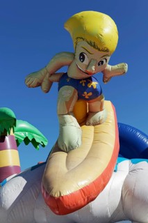 Inflatable bouncy castle with cartoon character Surfer on the beach