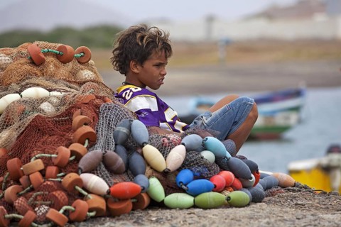 Young creole boy resting against pile of fishing nets in the harbour of fishing village Palmeira on the island of Sal