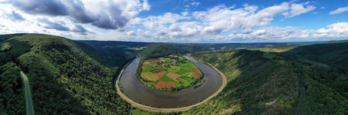 River bend of the Saar. The river winds through the valley and is surrounded by green hills and forests. Serrig