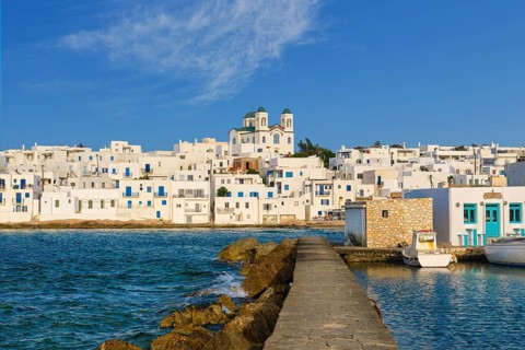 Traditional Greek whitewashed houses and church of Dormition of Mother of God as local landmark on hilltop by seafront on sunny day
