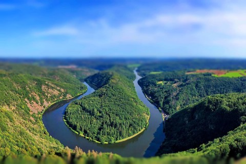 Aerial view of the Saar Loop. The Saar winds through the valley and is surrounded by green forests. Orscholz