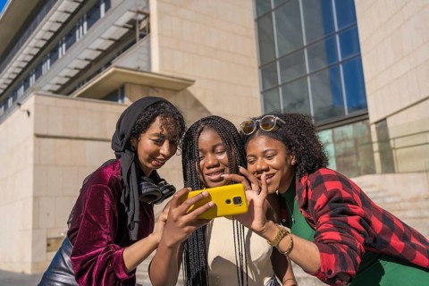 Curious multi-ethnic friends using mobile in the street in the city