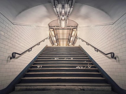 Subway corridor with white tile on walls and glowing lights above a the stairs passage. Symmetrical underground staircase