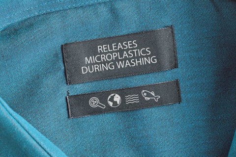Clothing label saying 'Releases microplastics during washing'. Concept for synthetic clothing fiber pollution problem