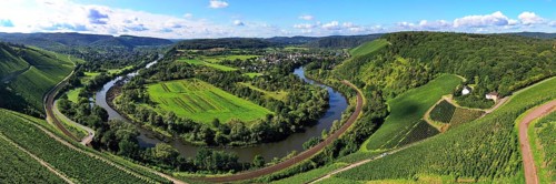 Wiltinger Saarbogen. The river winds through the valley and is surrounded by vineyards and green forests. Kanzem