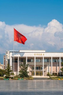 Palace of Culture or Opera on Skanderbeg Square in Tirana and the flag of Albania moving in the wind