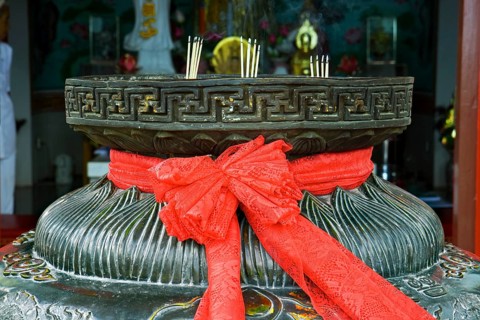 Red ribbon on a bowl for incense sticks in front of a pagoda