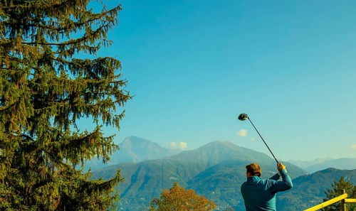 Golfer Teeing Off with His Driver with Mountain View in Autumn in Lombardy