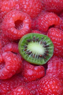 Halved mini kiwi on raspberries