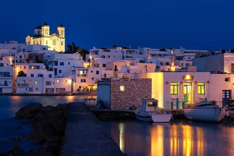 Traditional Greek whitewashed houses and church of Dormition of Mother of God on hilltop by seafront after sunset