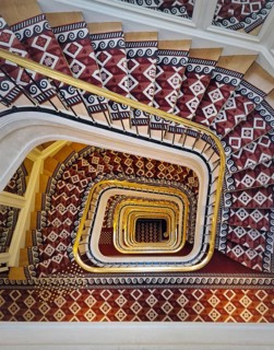 Abstract shape luxurious stairs with red carpet cover and golden handrail. Hypnotic pattern spiral staircase