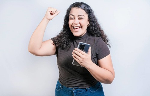 Winning happy young woman holding cell phone. Happy latin girl celebrating with phone isolated. Happy people holding smartphone and celebrating