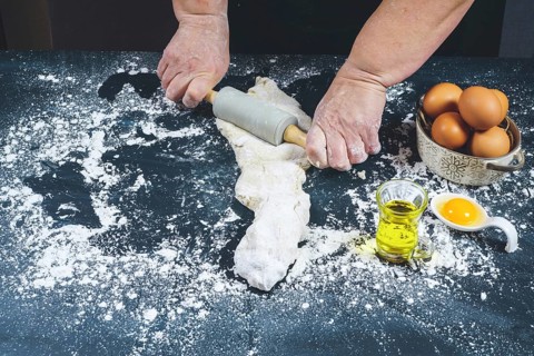 Woman kneading with a rolling pin a dough of flour to make bread on a black wooden table with olive oil