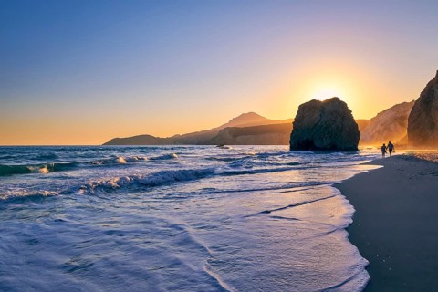 Distant silhouettes of two adults walking in tidal waters on Fyriplaka beach