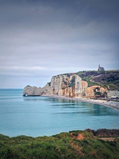 Idyllic view to Etretat coastline with the famous Notre-Dame de la Garde chapel on the Amont cliff. Shore washed by Atlantic ocean waters