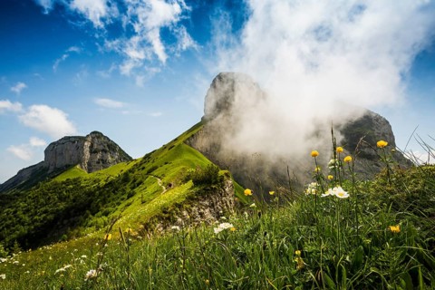Steep mountains and clouds and flower meadow