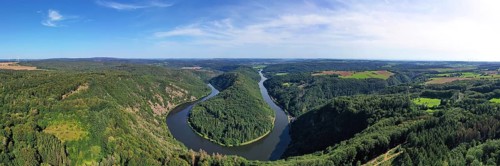 Aerial view of the Saar Loop. The Saar winds through the valley and is surrounded by green forests. Orscholz