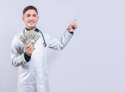 Happy latin doctor holding money and pointing to side. Handsome smiling doctor showing money and pointing side