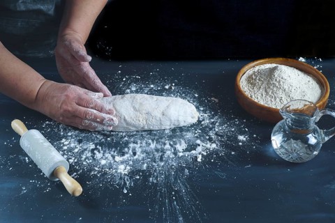 Woman kneading with her hands a flour dough to make homemade bread on a black wooden table with flour